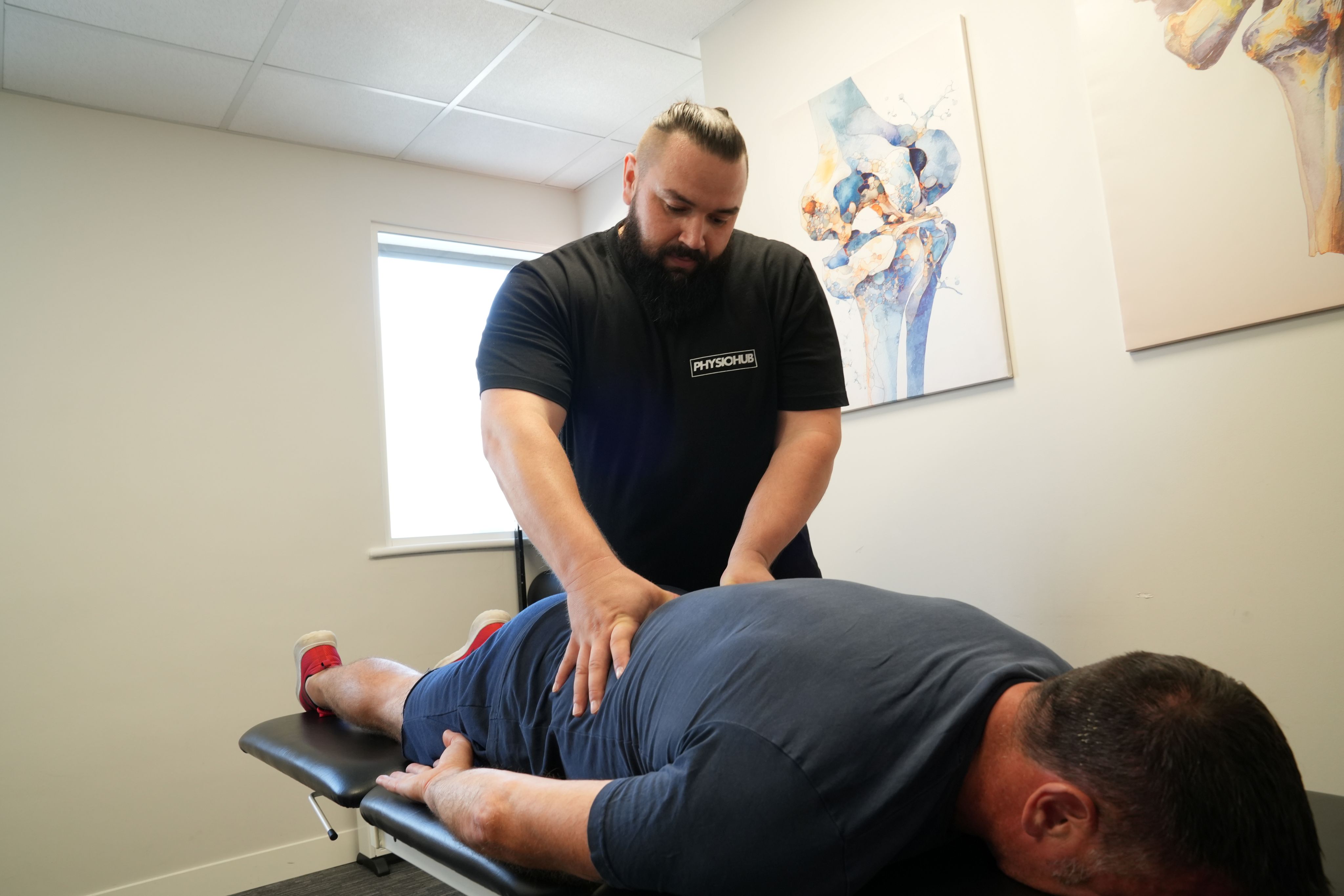 Massage therapist using forearm pressure along a client's back on a treatment couch