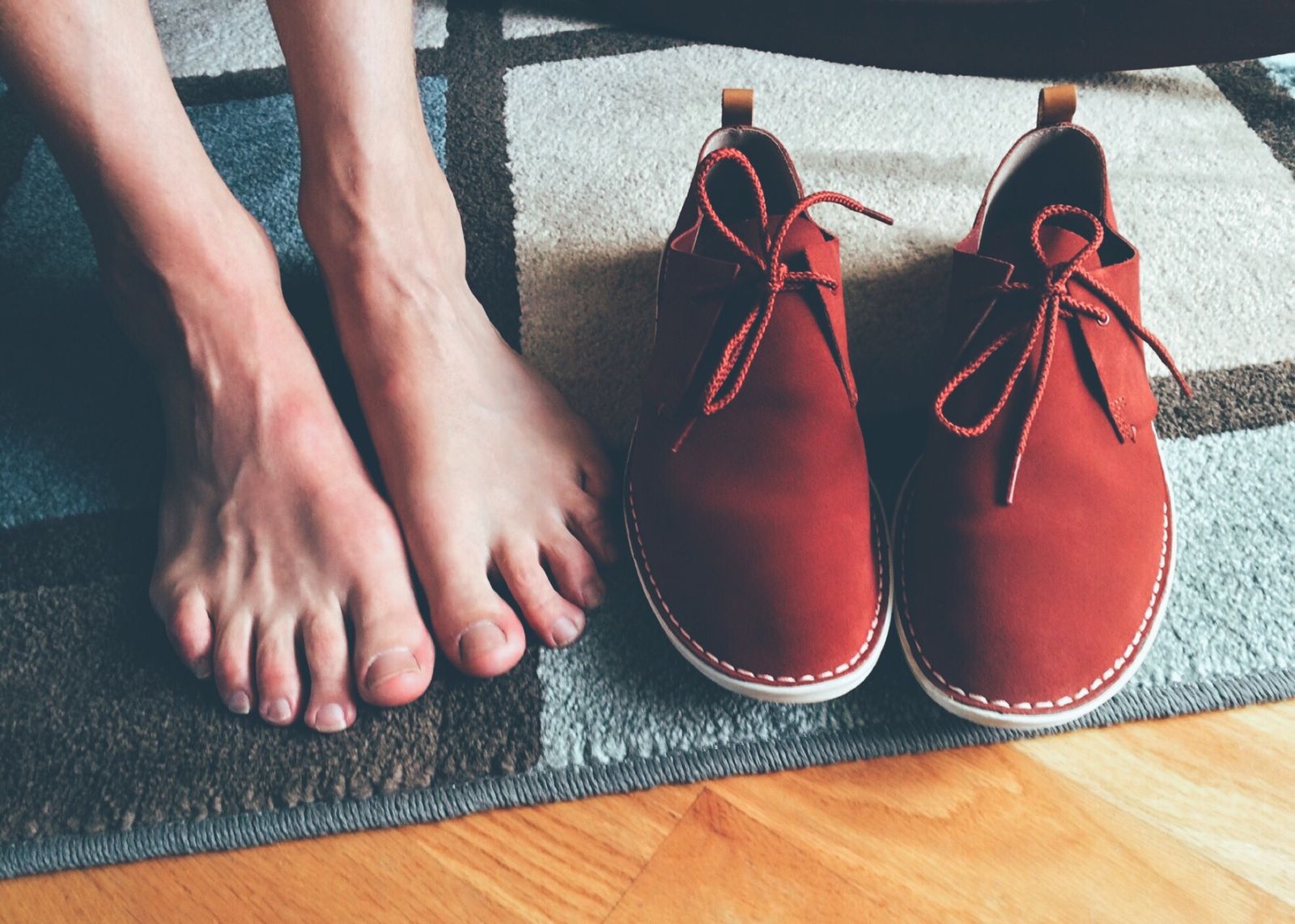 Bare feet on a rug beside a pair of shoes
