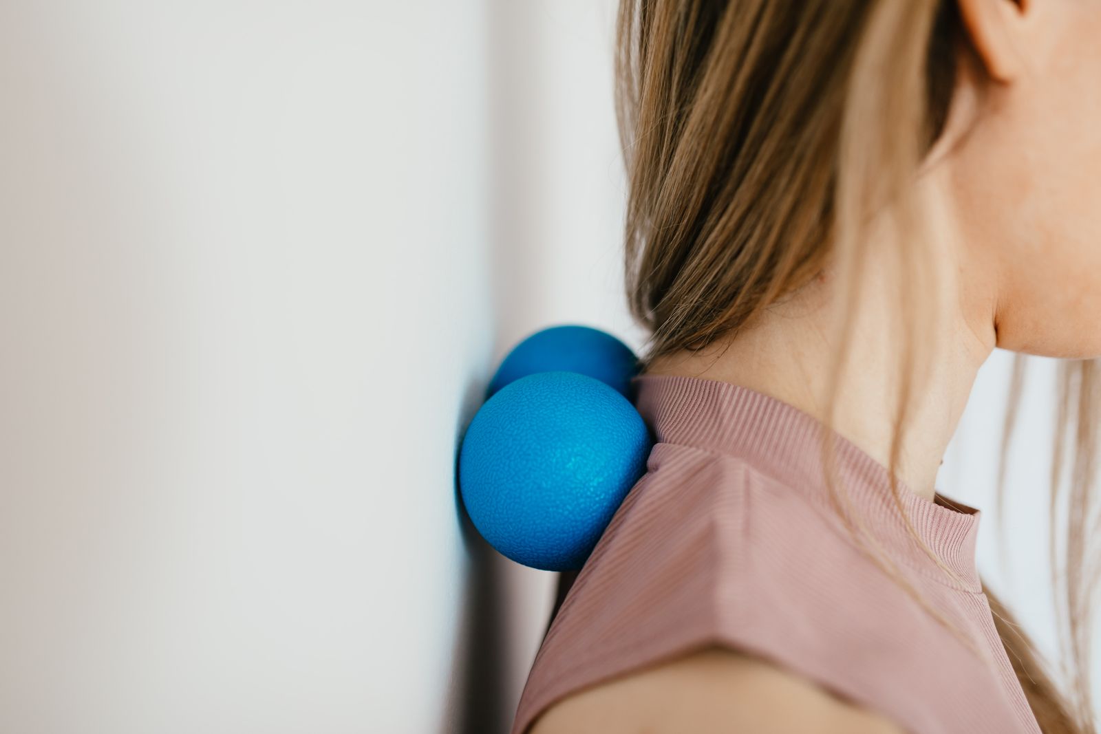 Person easing tension between the shoulder blades with a massage ball against a wall