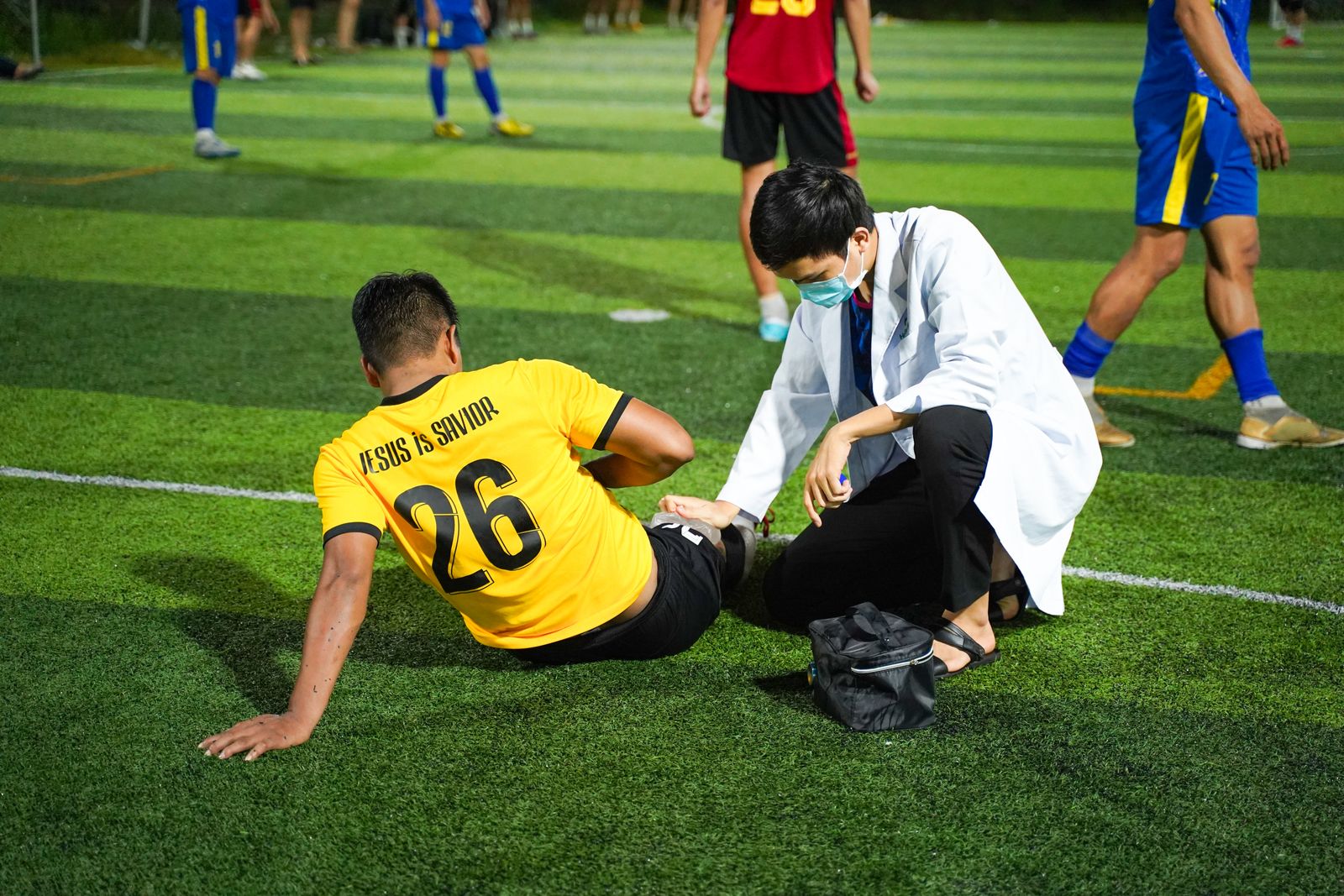 Pitch-side medic treating an injured footballer's leg during a match