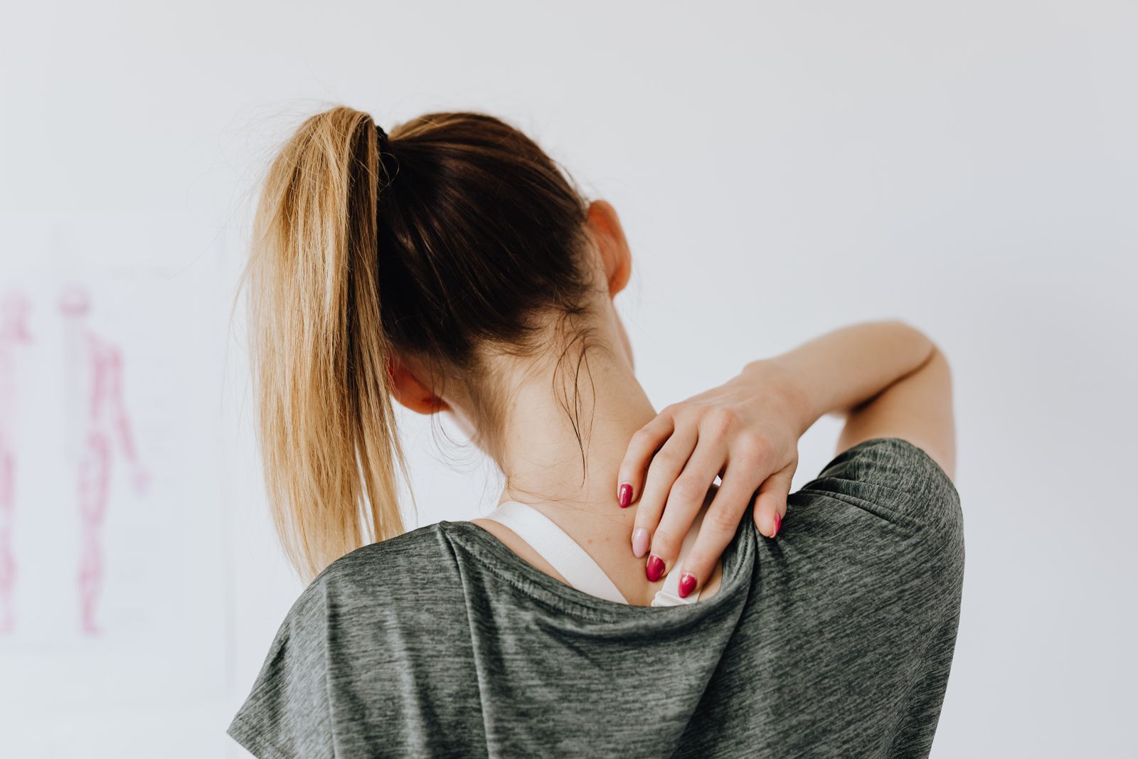 Person reaching back to a tight, painful muscle at the base of the neck