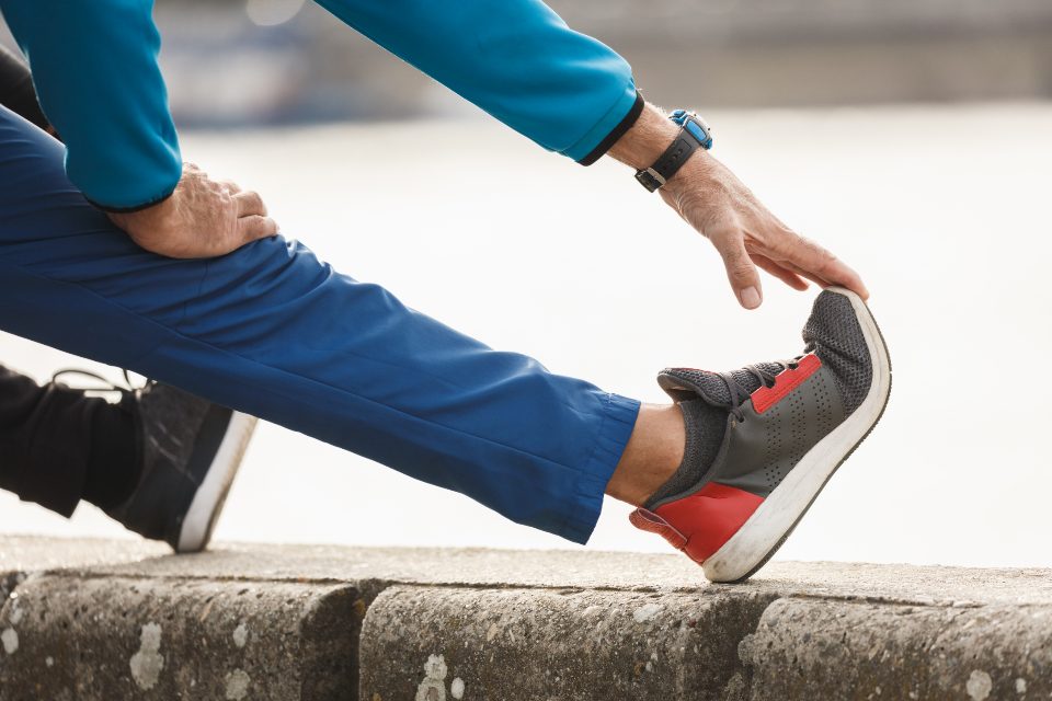 A man stretching his calf with one foot pressed against a wall