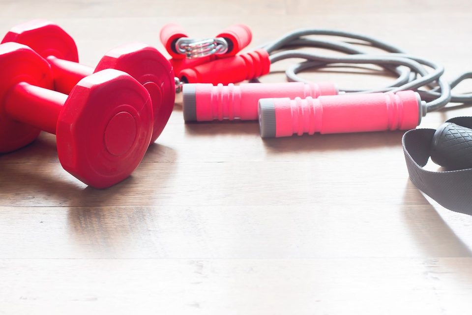 A pair of red dumbbells and a skipping rope on a wooden floor
