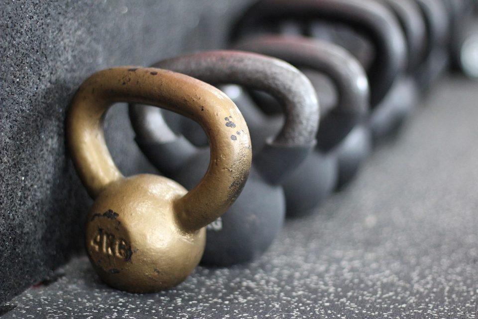 A brass kettlebell on a gym floor with a row of heavier bells behind it