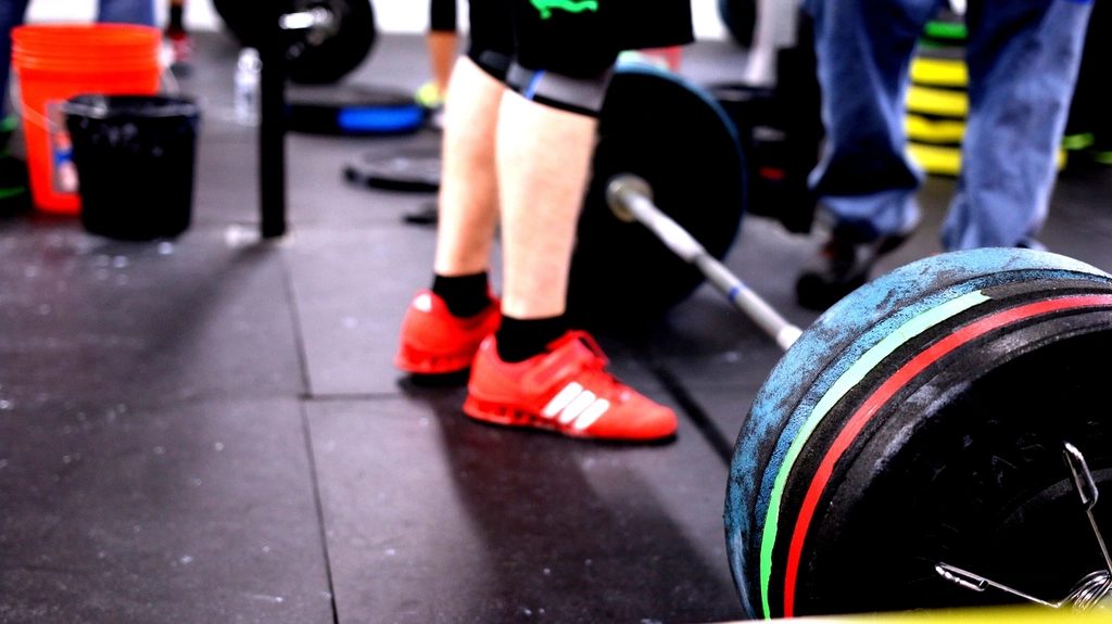 A loaded barbell on a gym floor beside a lifter's feet