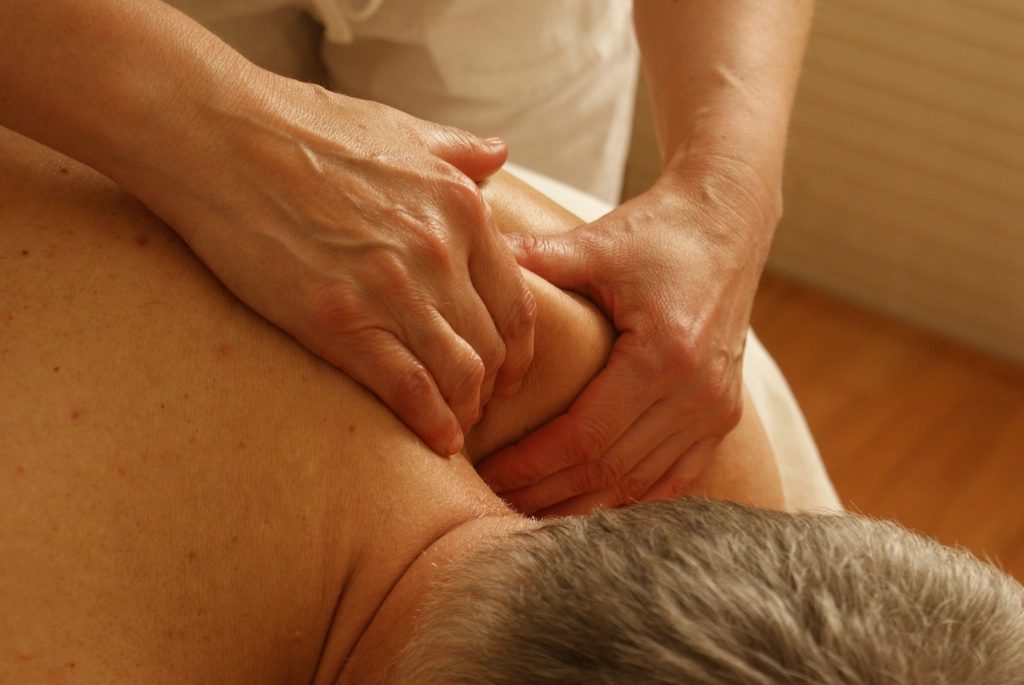 A therapist's hands working into the muscles of a patient's upper back and neck