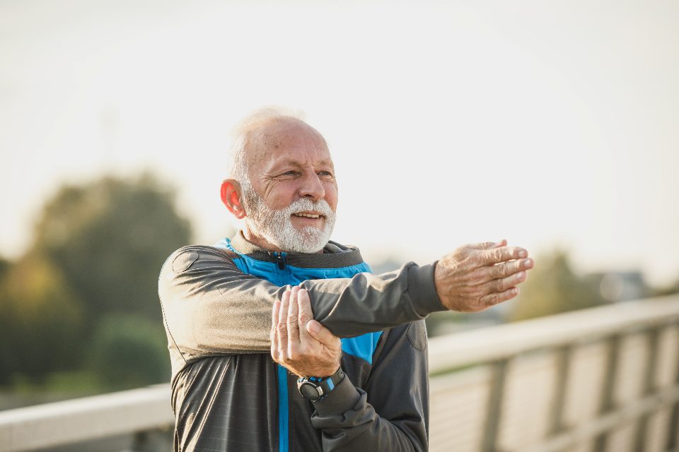 An older man stretching his arms across his chest outdoors