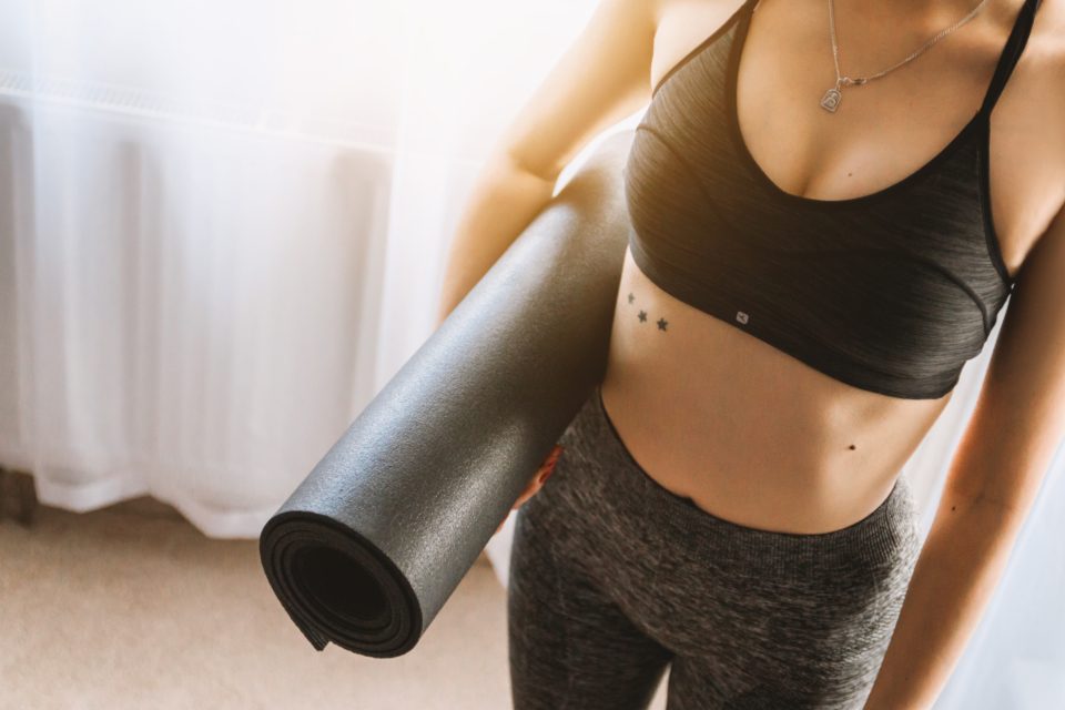 A person holding a rolled exercise mat under one arm