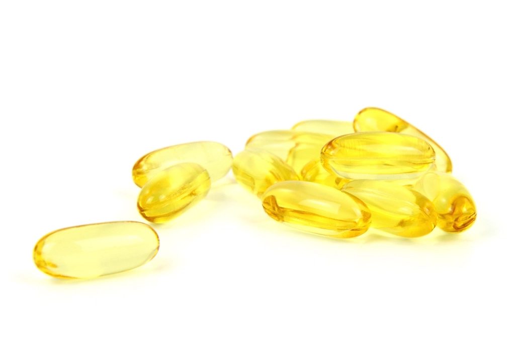 A small pile of yellow softgel capsules on a white surface